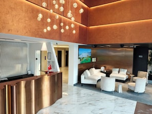 A modern lobby with a reception desk, seating area, and a large screen displaying a landscape. - The Corner Park Hotel (Konyaalti)
