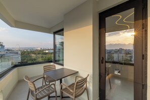 A balcony with a table and chairs, a glass door, and a view of a cityscape with buildings and a Ferris wheel.