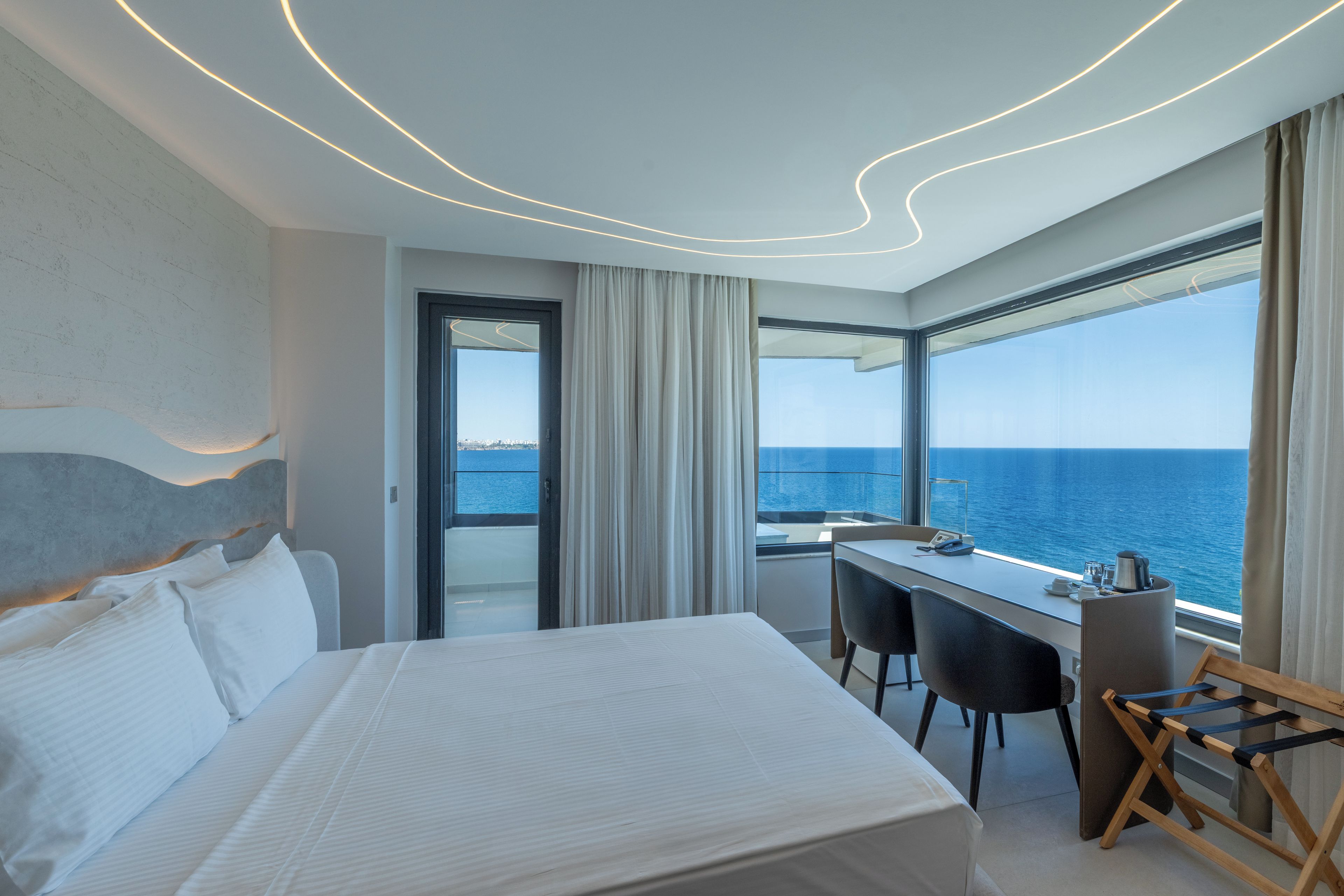 Quarto de hotel moderno com uma cama grande, uma mesa de trabalho e vista para o mar.