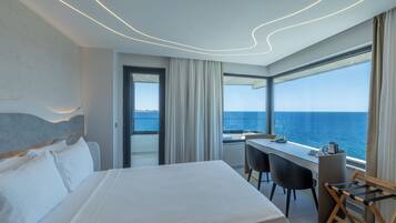 Quarto de hotel moderno com uma cama grande, uma mesa de trabalho e vista para o mar.