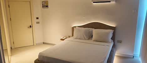 A hotel room with a bed, bedside table, and an air conditioning unit.