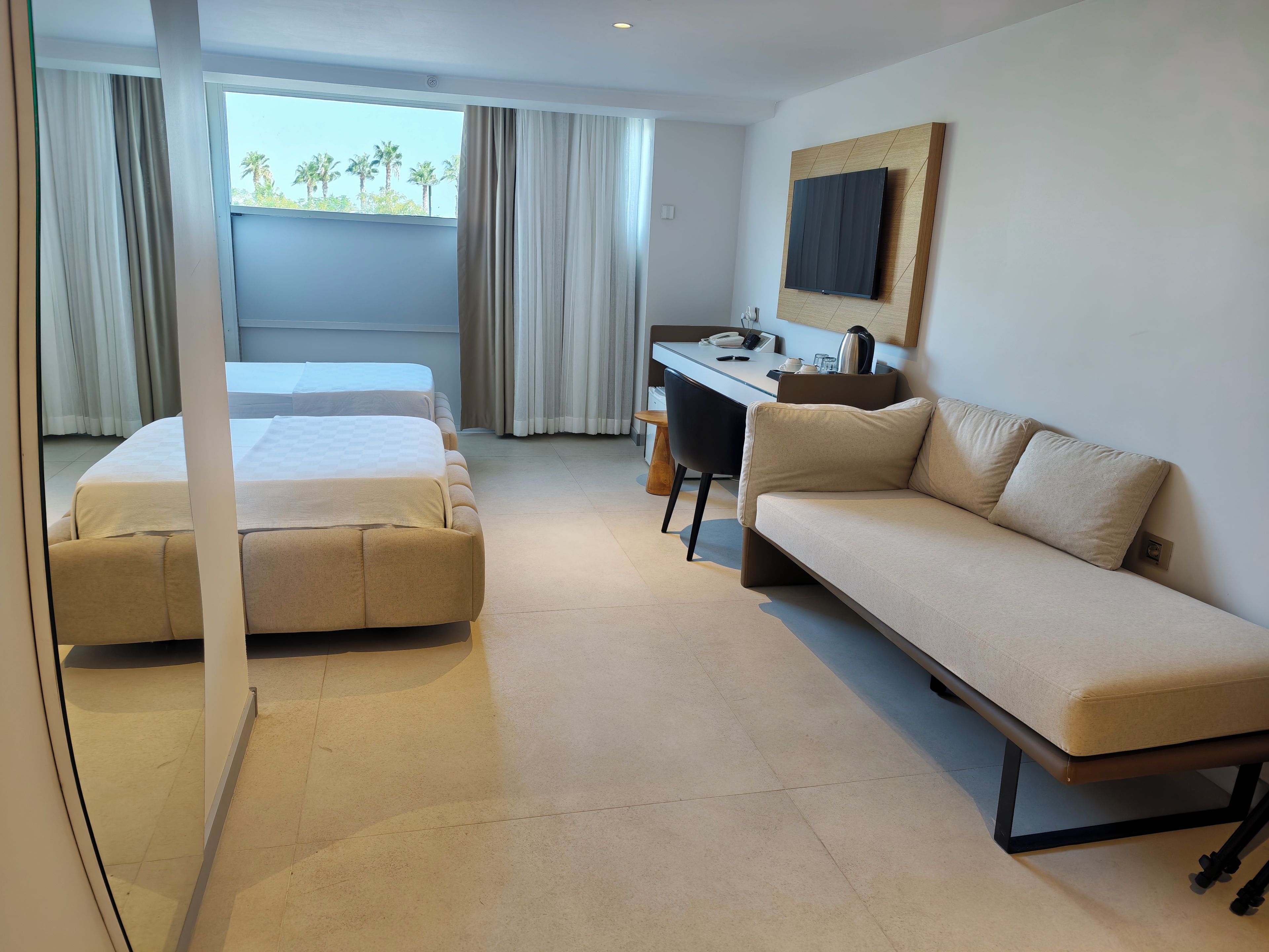 A hotel room with a bed, a sofa, a desk, and a large window with curtains.