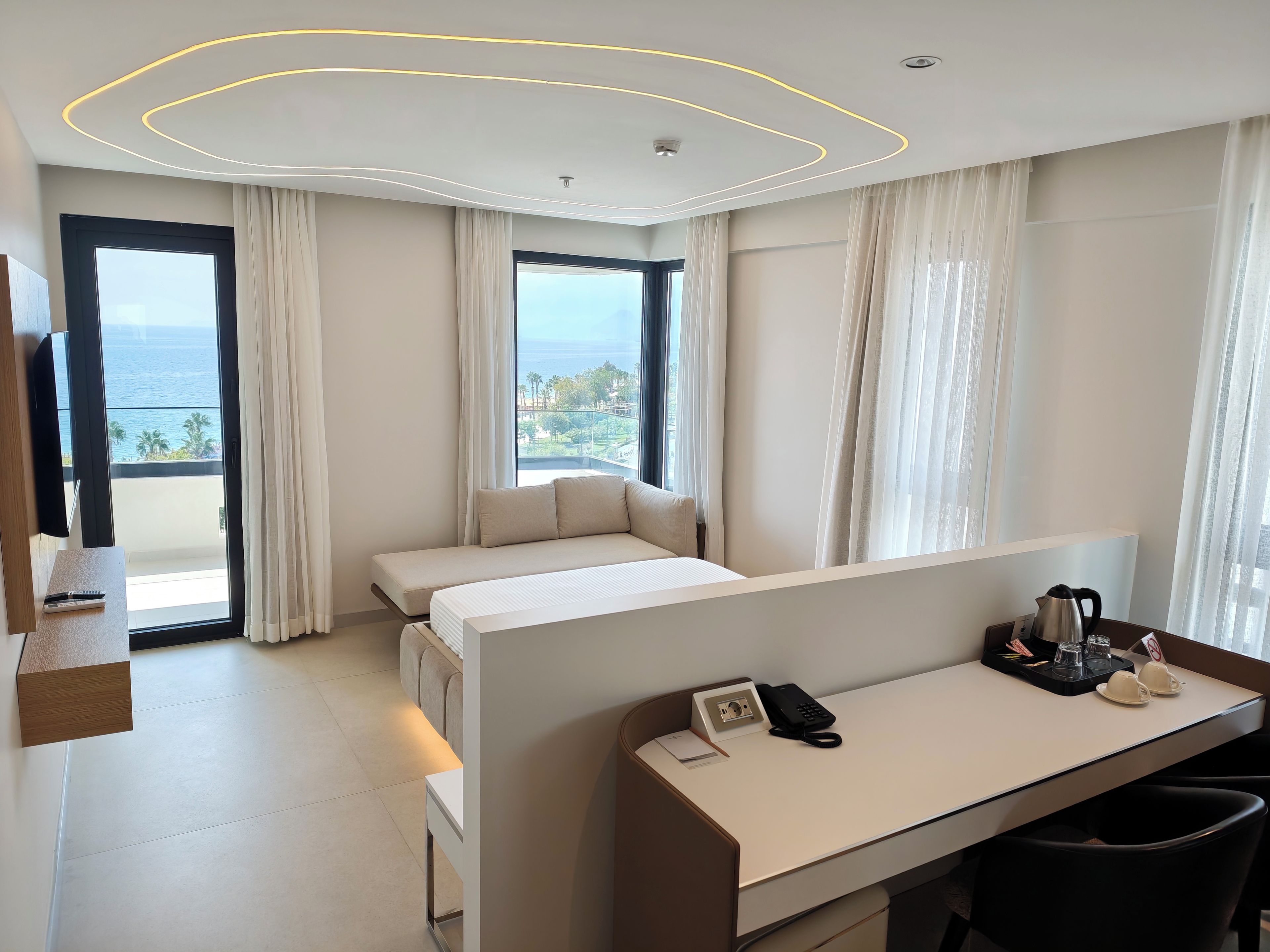 A modern hotel room with a bed, a desk, a telephone, a coffee maker, and a view of the ocean.