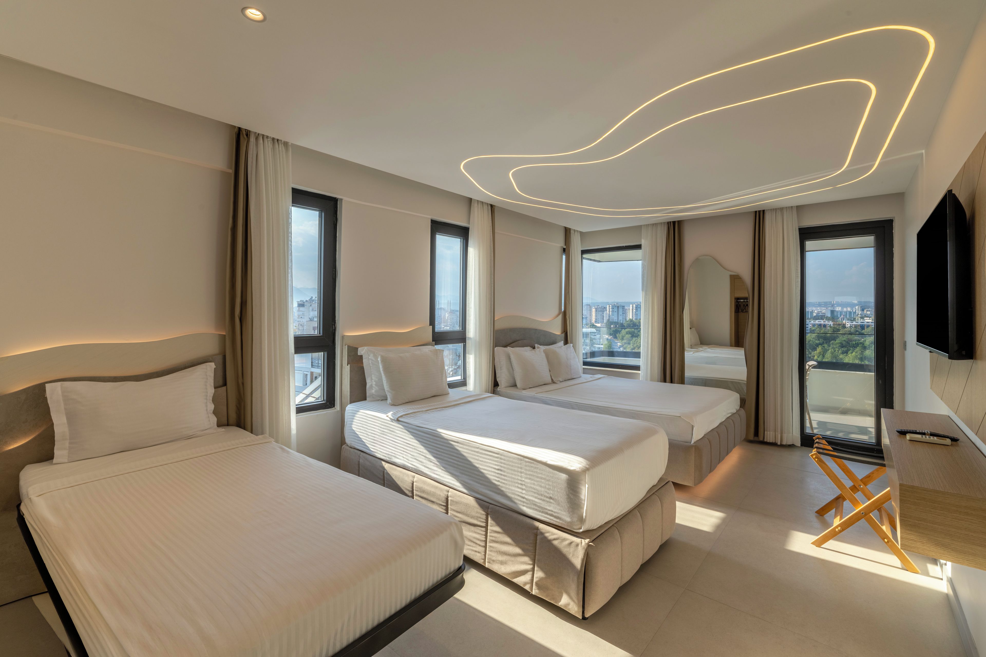 Quarto de hotel moderno com duas camas, uma janela ampla com vista para a cidade e uma TV de tela plana na parede.