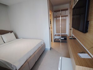 Una habitación de hotel moderna con una cama grande, un escritorio de madera y un televisor montado en la pared.