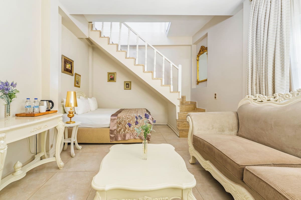 Une chambre d’hôtel avec un escalier, un lit, un canapé, une table basse et un bureau doté d’une lampe et d’objets décoratifs.