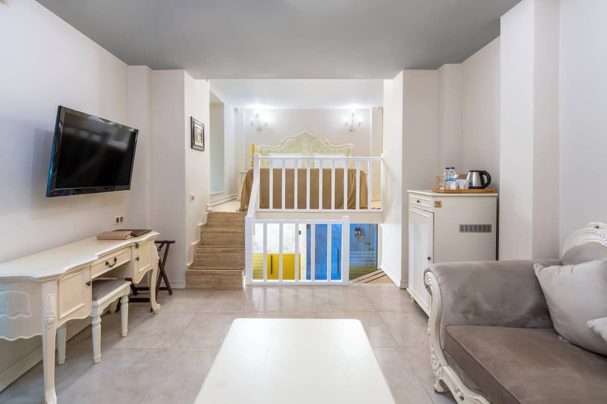 Un salon comprenant un téléviseur, un bureau, un canapé, un escalier et un coin cuisine.