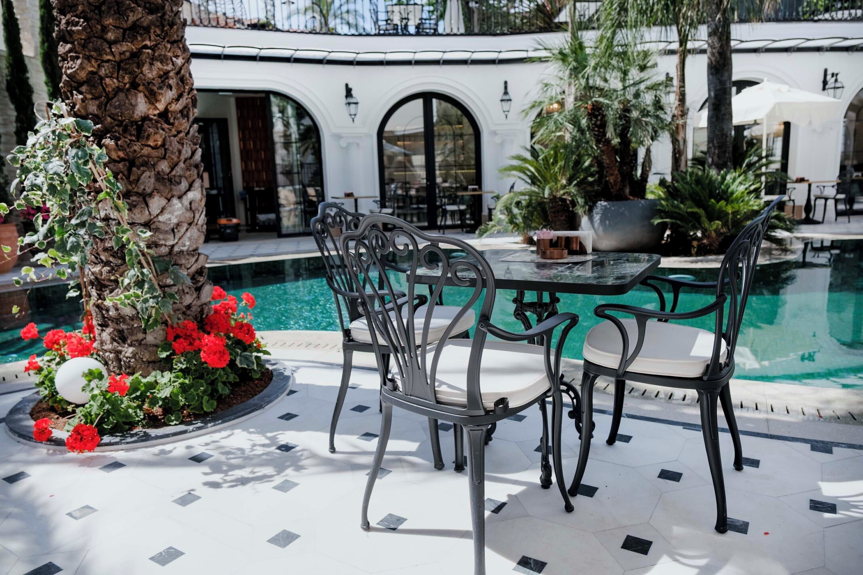 A poolside area with a table and chairs, a palm tree, and a pool.