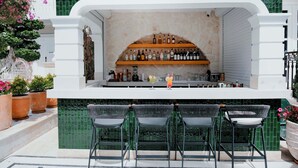 Een bar met een stenen muur, flessen op planken en drie barkrukken.
