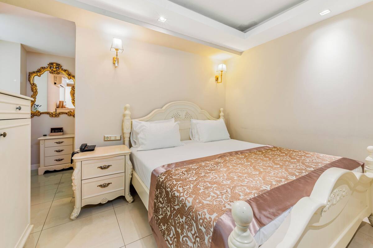 Une chambre à coucher comprenant un lit, des tables de chevet, une commode, un miroir et des appliques murales.