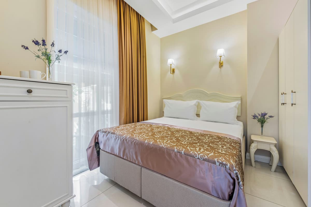 Une chambre d’hôtel avec un lit, une commode, une table de chevet et une fenêtre avec des rideaux.