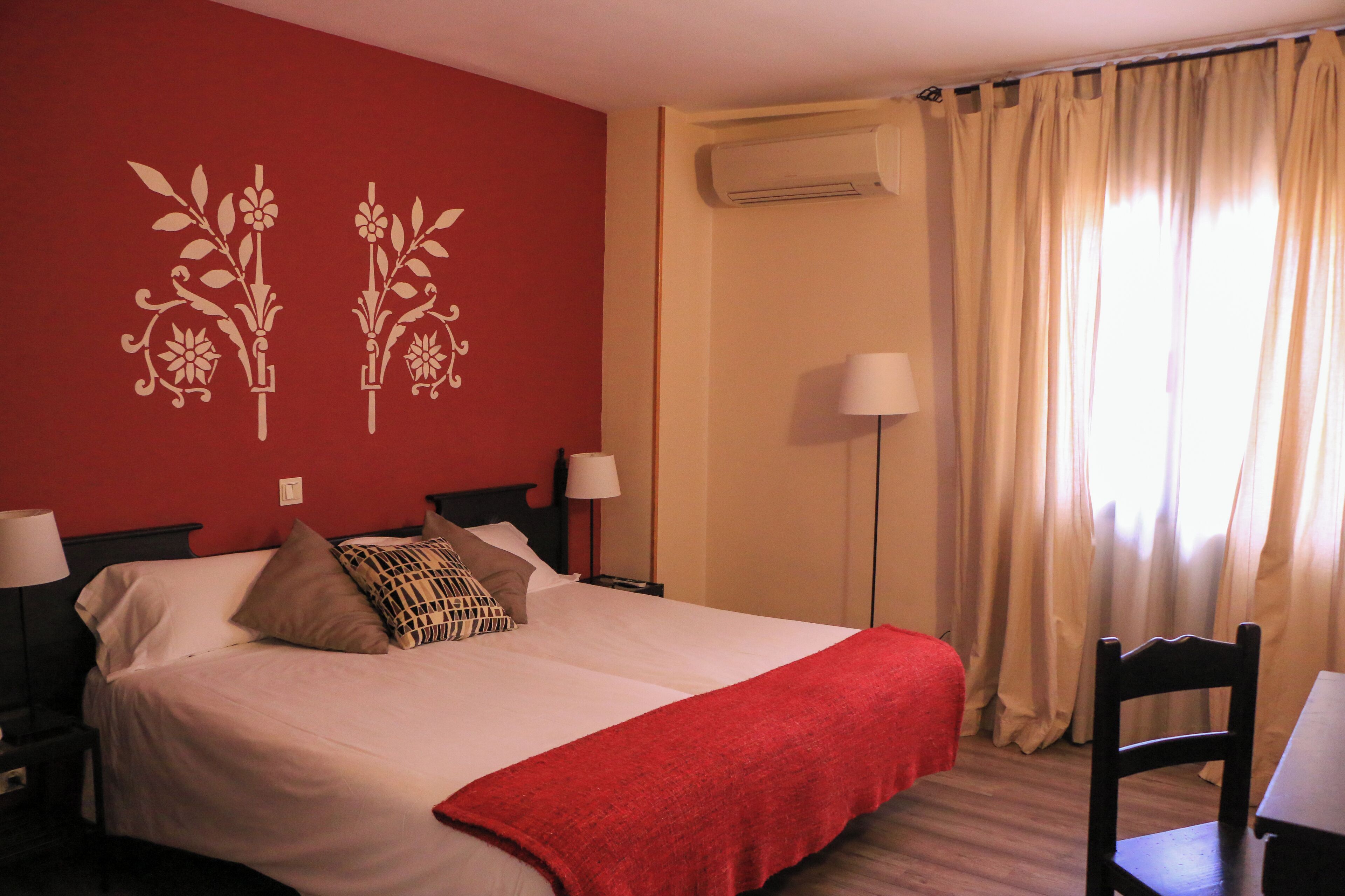 Een hotelkamer met een bed, een bureau, een stoel, een lamp en een raam met gordijnen.