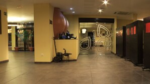 Un vestíbulo de hotel con una recepción, una gran escultura abstracta y vistas al comedor.