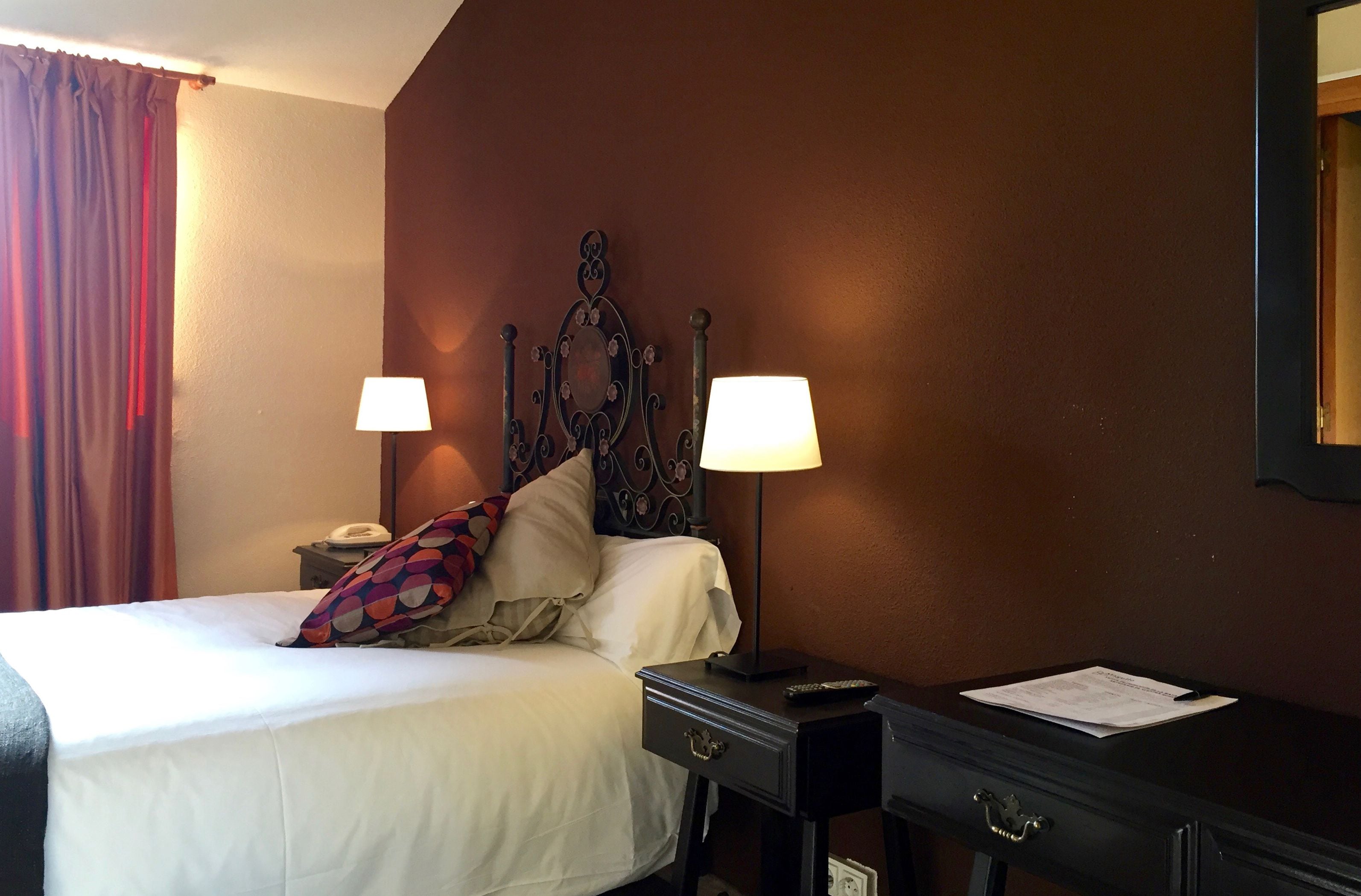 A hotel room with a bed, two bedside lamps, a nightstand, a dresser, and a mirror on the wall.