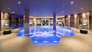 Una amplia piscina interior con suelo iluminado en azul, rodeada de sillones de descanso y un diseño de interiores moderno.