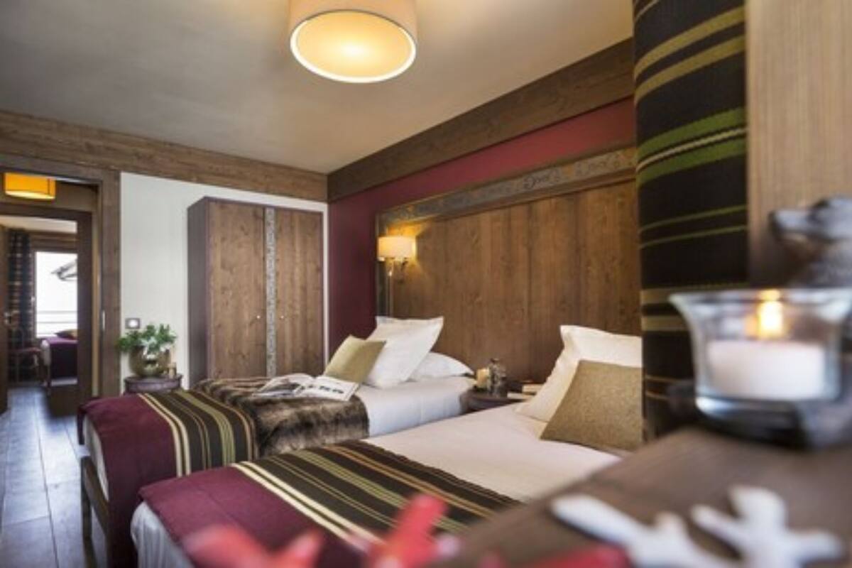 A hotel room with two beds, wooden headboards, a nightstand with a lamp, and a view of the hallway.