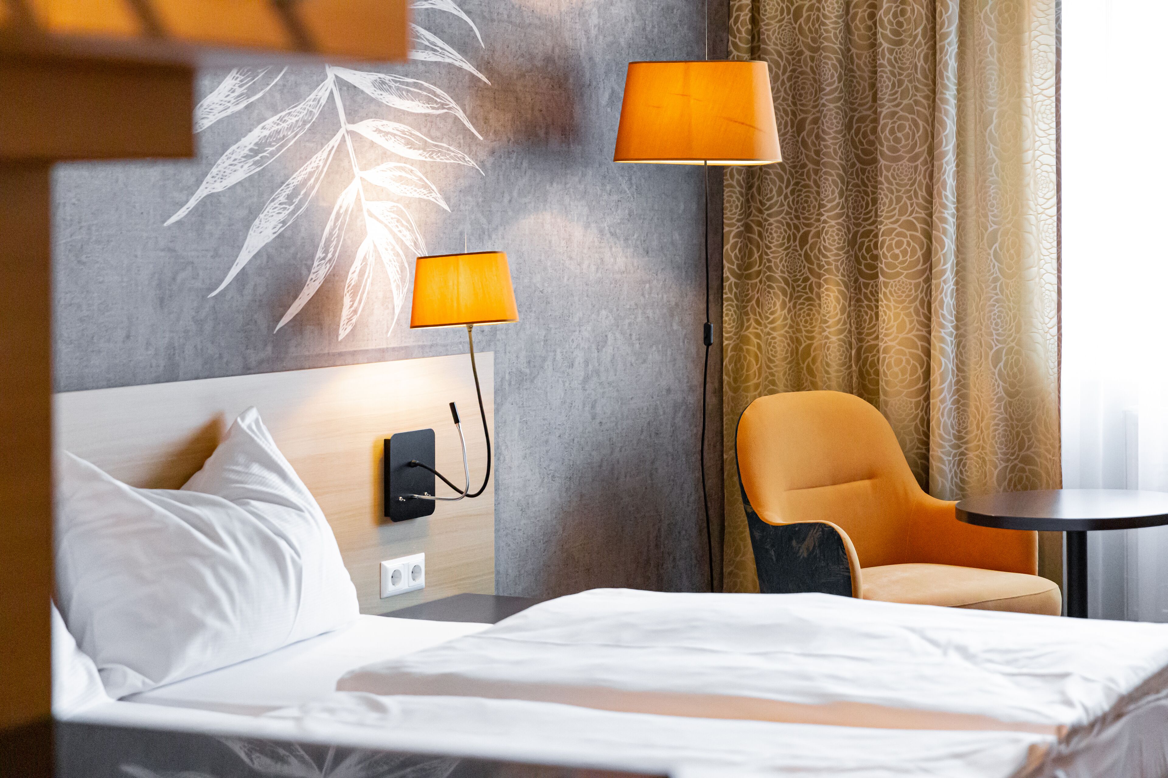 A hotel room with a bed, two lamps, a chair, and a table.