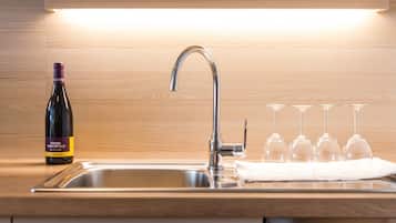 Una cocina con un lavamanos de acero inoxidable, una botella de vino y copas de vino sobre la encimera.