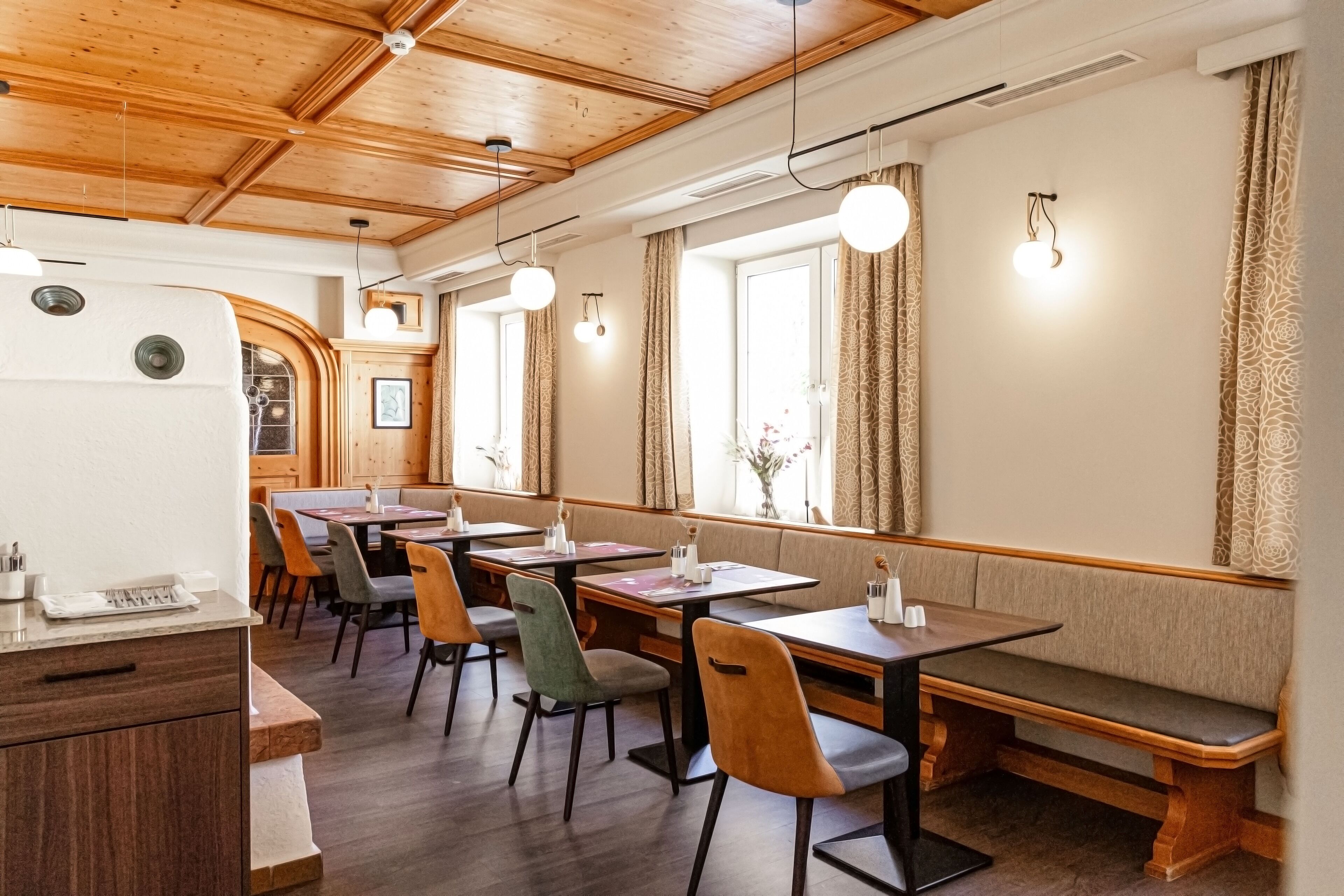 A restaurant with wooden ceiling beams, large windows with curtains, and multiple tables and chairs.