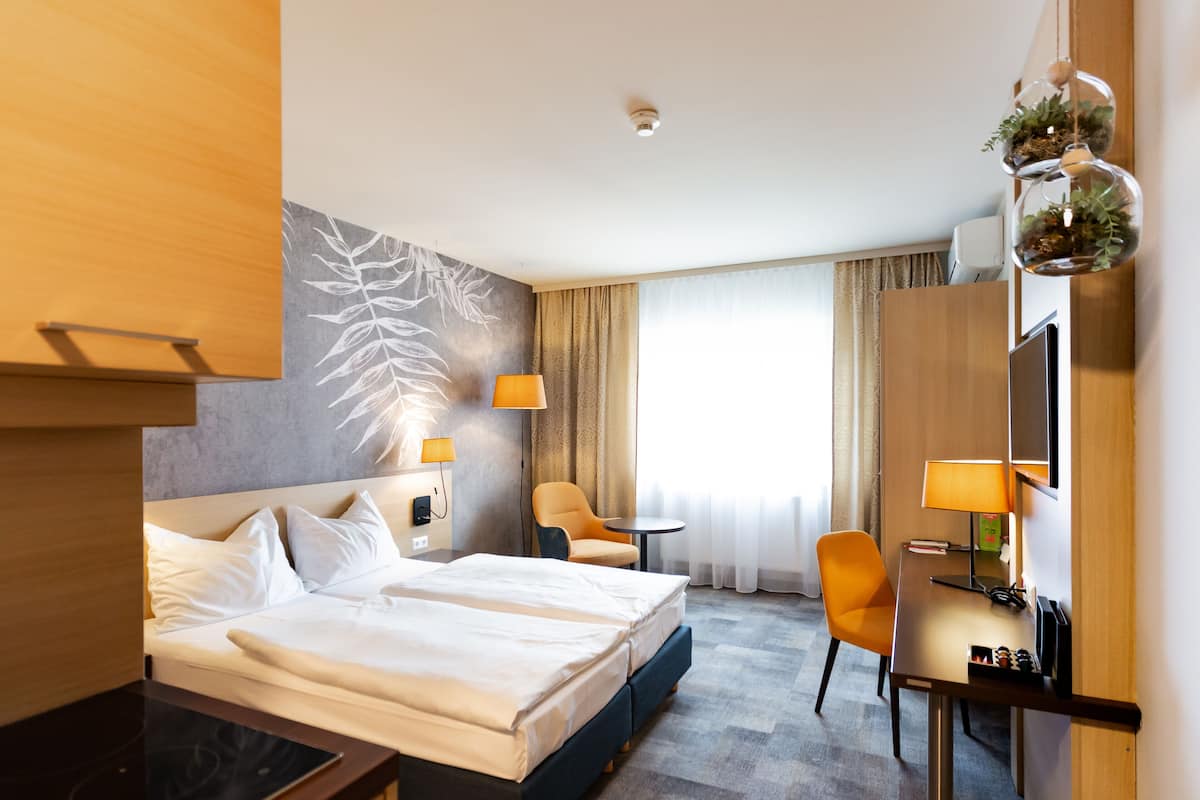 A hotel room with a bed, a desk, a chair, and a large window with curtains.