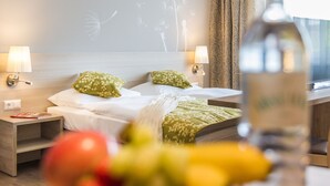 Habitación de hotel con dos camas, almohadas estampadas con motivos florales, lámparas de noche, una mesita de noche y una botella de agua sobre la mesa.