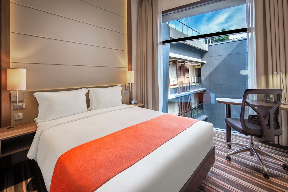 Habitación de hotel con una cama grande, un escritorio y vistas a un balcón.