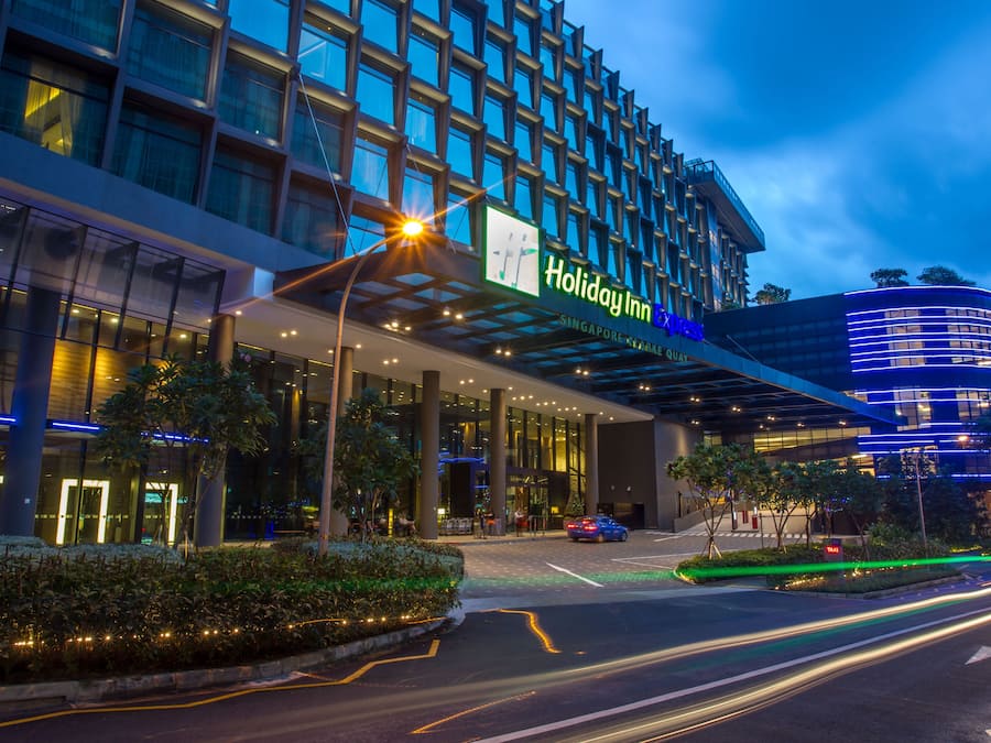 A Holiday Inn Express building with a modern glass facade, a covered entrance, and a landscaped area with trees and shrubs.