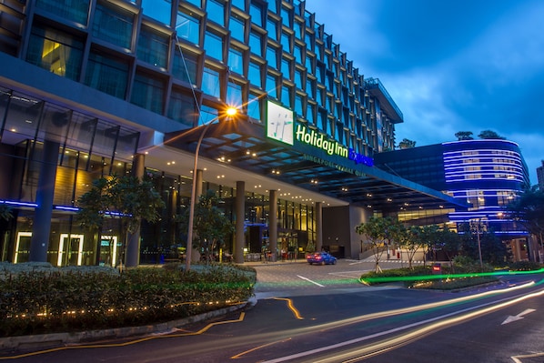A Holiday Inn Express building with a modern glass facade, a covered entrance, and a landscaped area with trees and shrubs.