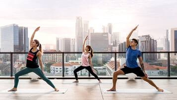 Three individuals performing yoga in a room with a cityscape view through large windows.