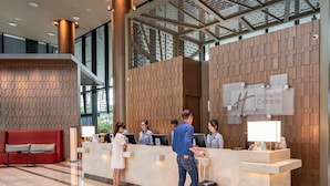 Et hotellets receptionområde med et moderne design, med en reception, en rød sofa og et stort vindue med udsigt over bybilledet.