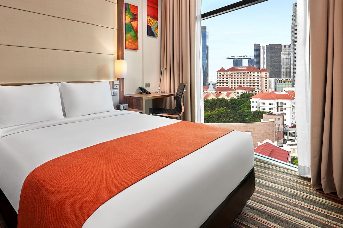 Habitación de hotel con una cama grande, un escritorio, una silla y vistas a la ciudad.