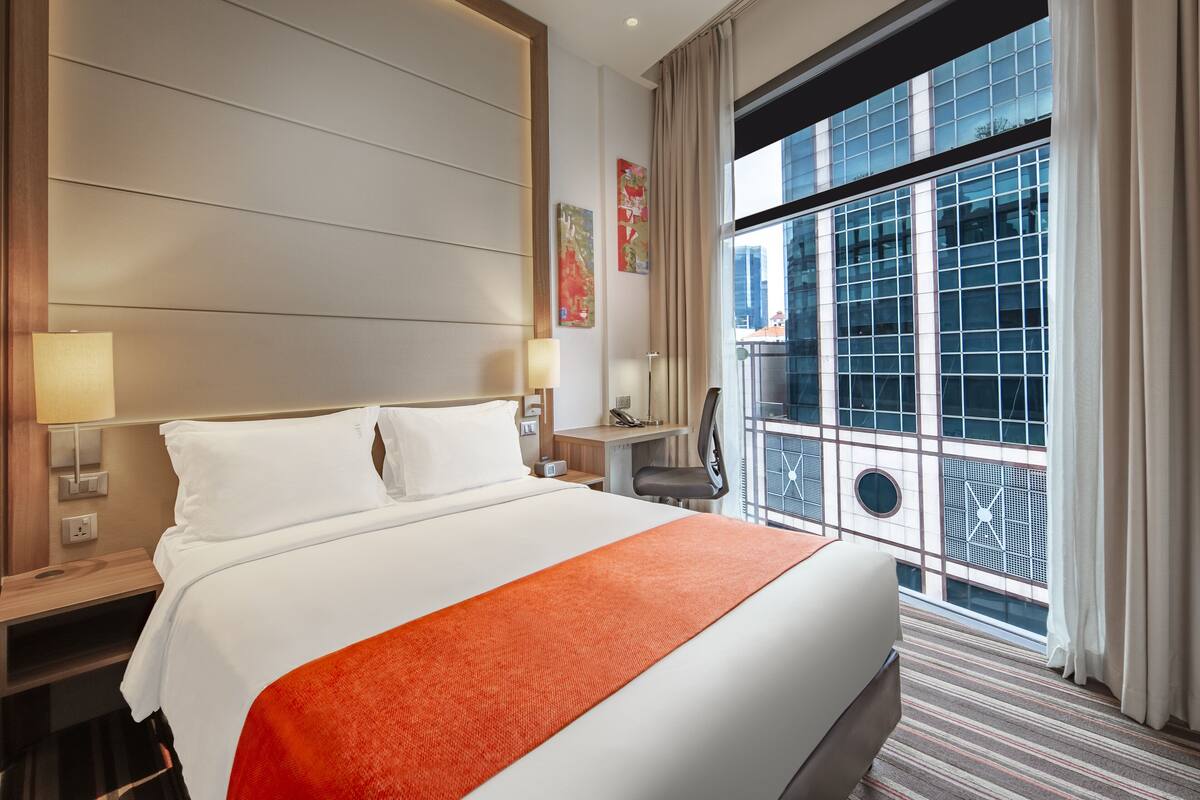 Una habitación de hotel con una cama grande, un escritorio y vistas de la ciudad a través de amplias ventanas.