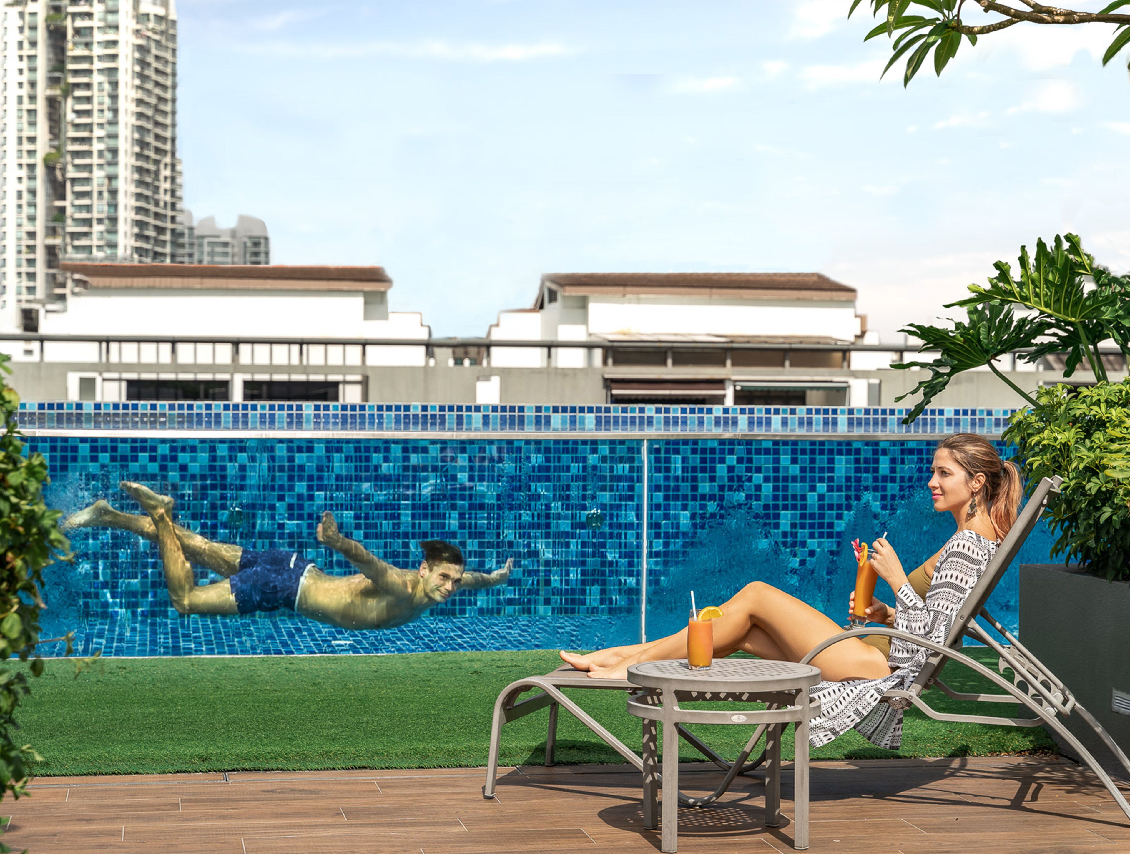 A swimming pool with a tiled blue border, a lounge chair, and a table with a drink.