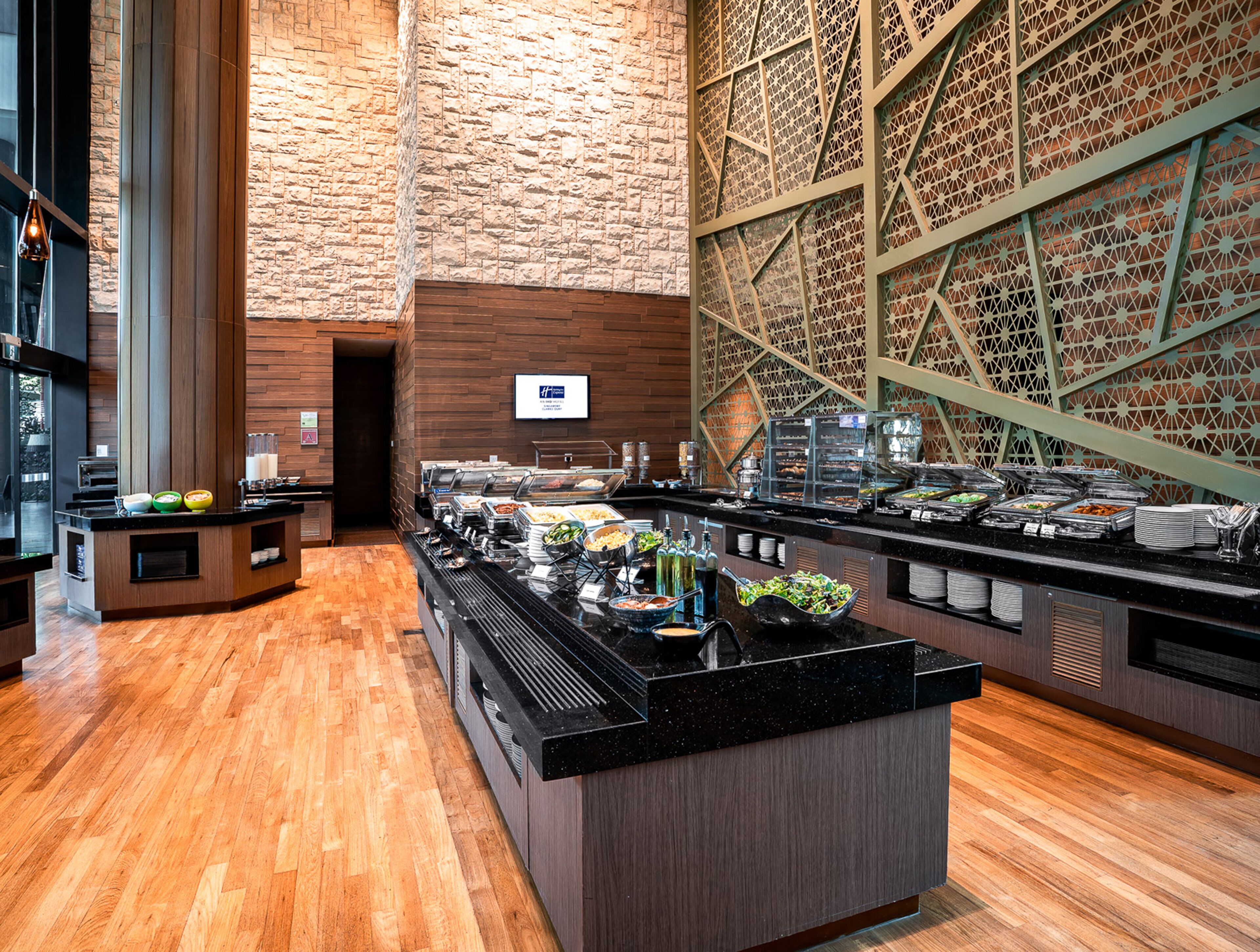 Zona de bufé con diversas opciones de comida, suelo de madera y pared de ladrillo con un diseño geométrico.