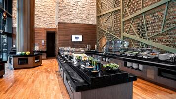 Zona de bufé con diversas opciones de comida, suelo de madera y pared de ladrillo con un diseño geométrico.