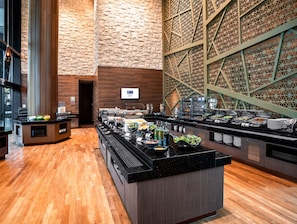 Zona de bufé con diversas opciones de comida, suelo de madera y pared de ladrillo con un diseño geométrico.