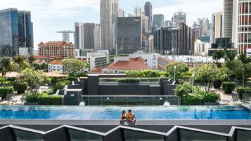 Una piscina en la azotea con vistas al horizonte urbano, rodeada de vegetación y arquitectura moderna.