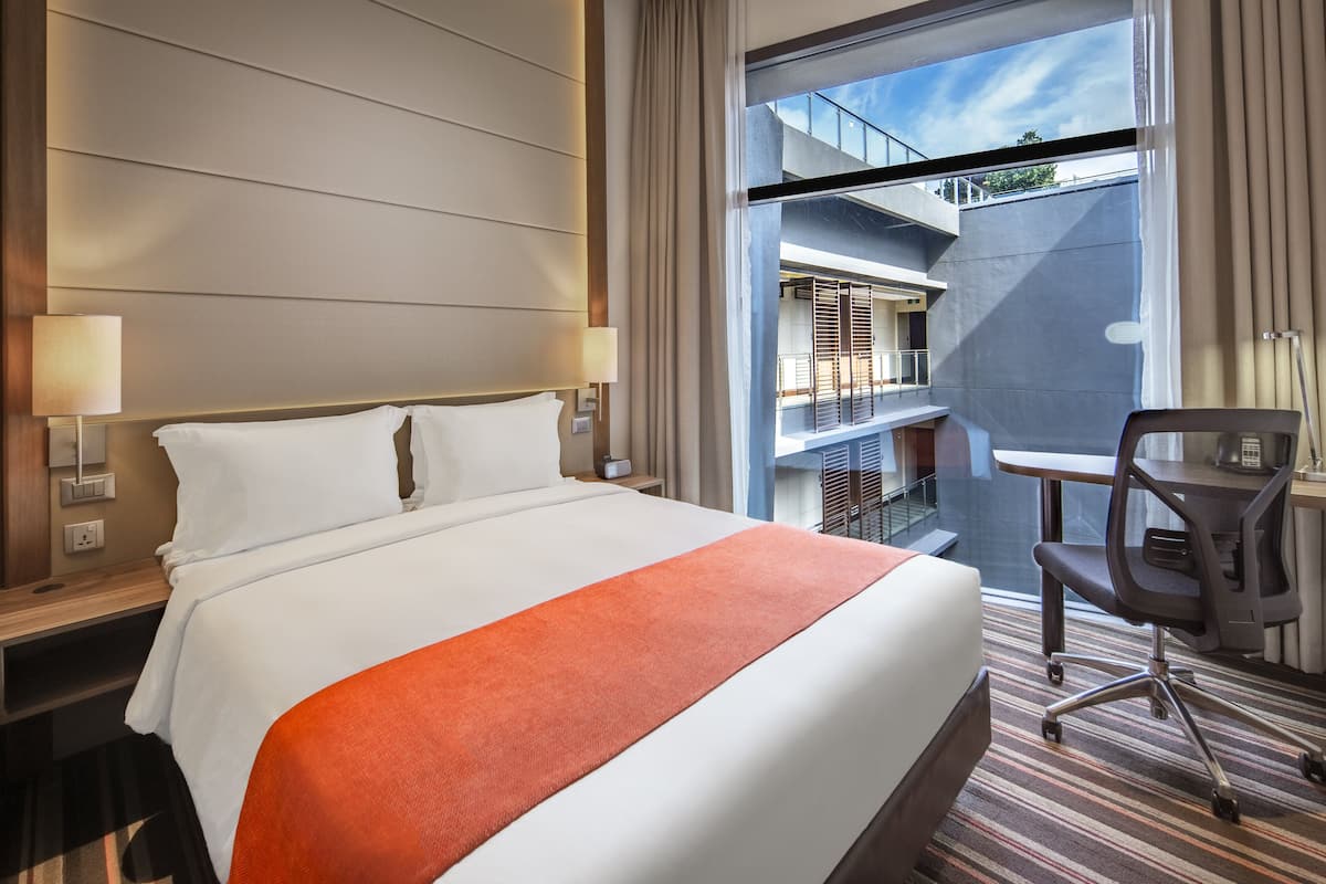 Habitación de hotel con una cama grande, un escritorio y vistas a un balcón.
