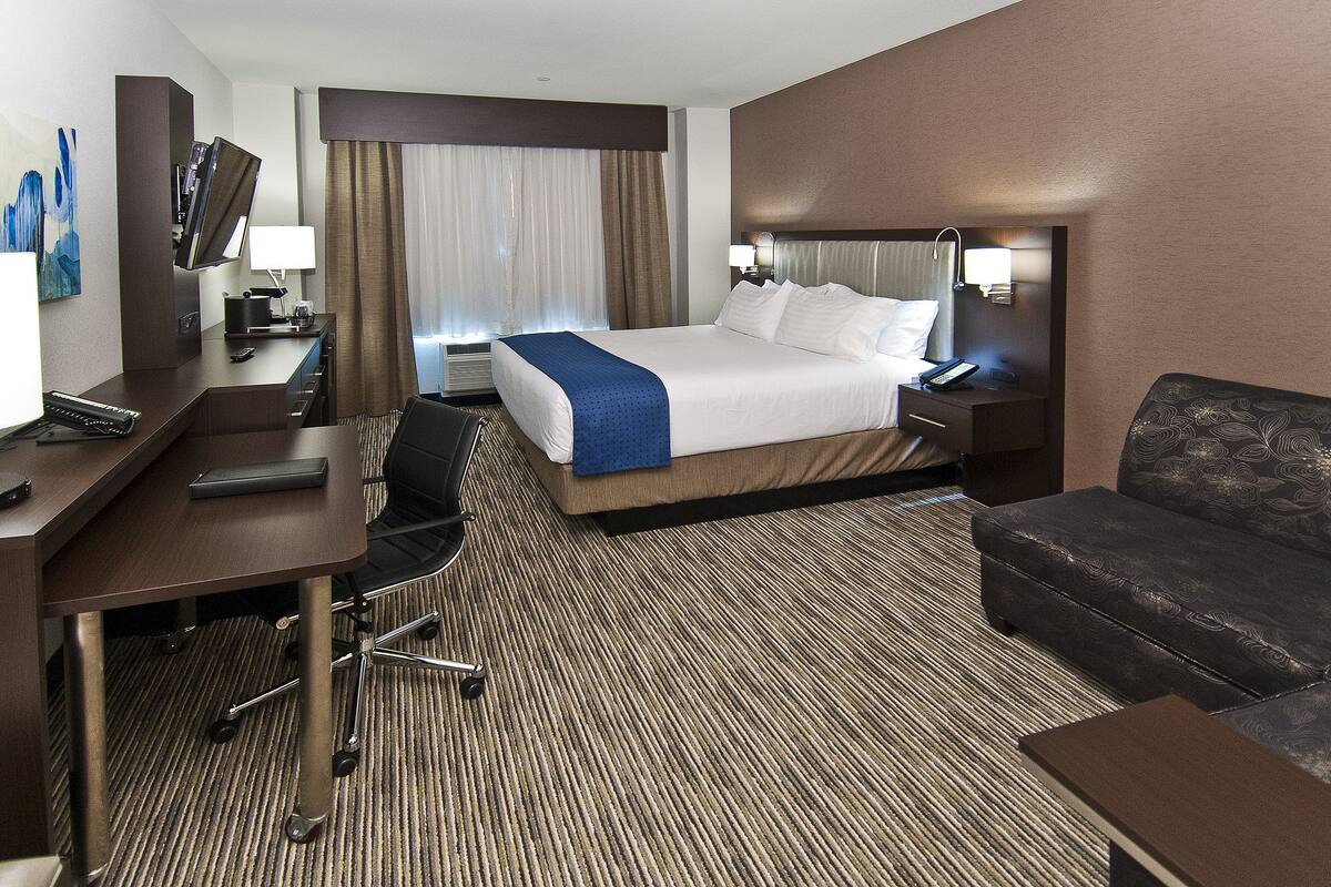 A hotel room with a bed, desk, chair, and a sofa.