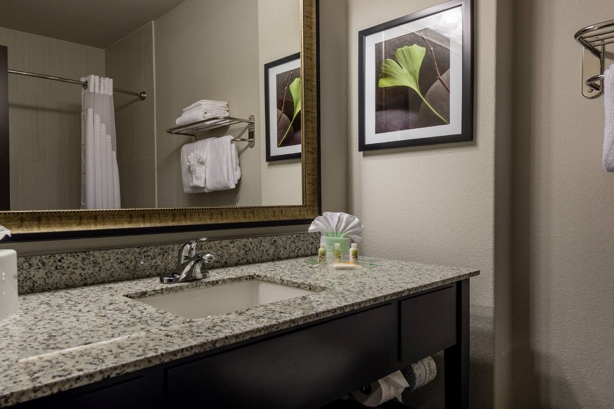 A bathroom with a granite countertop, a sink, a mirror, and framed pictures on the wall.