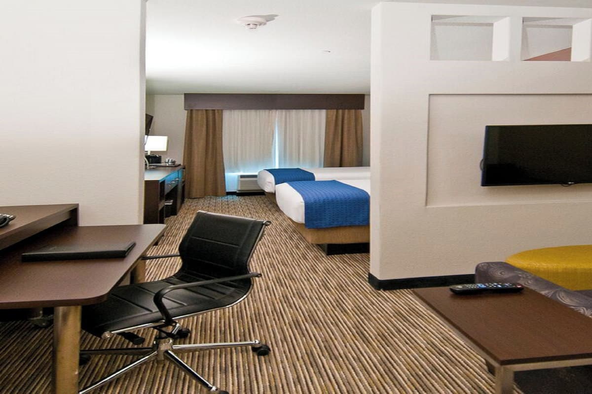 A hotel room with a bed, a desk, a chair, a television, and a sofa.