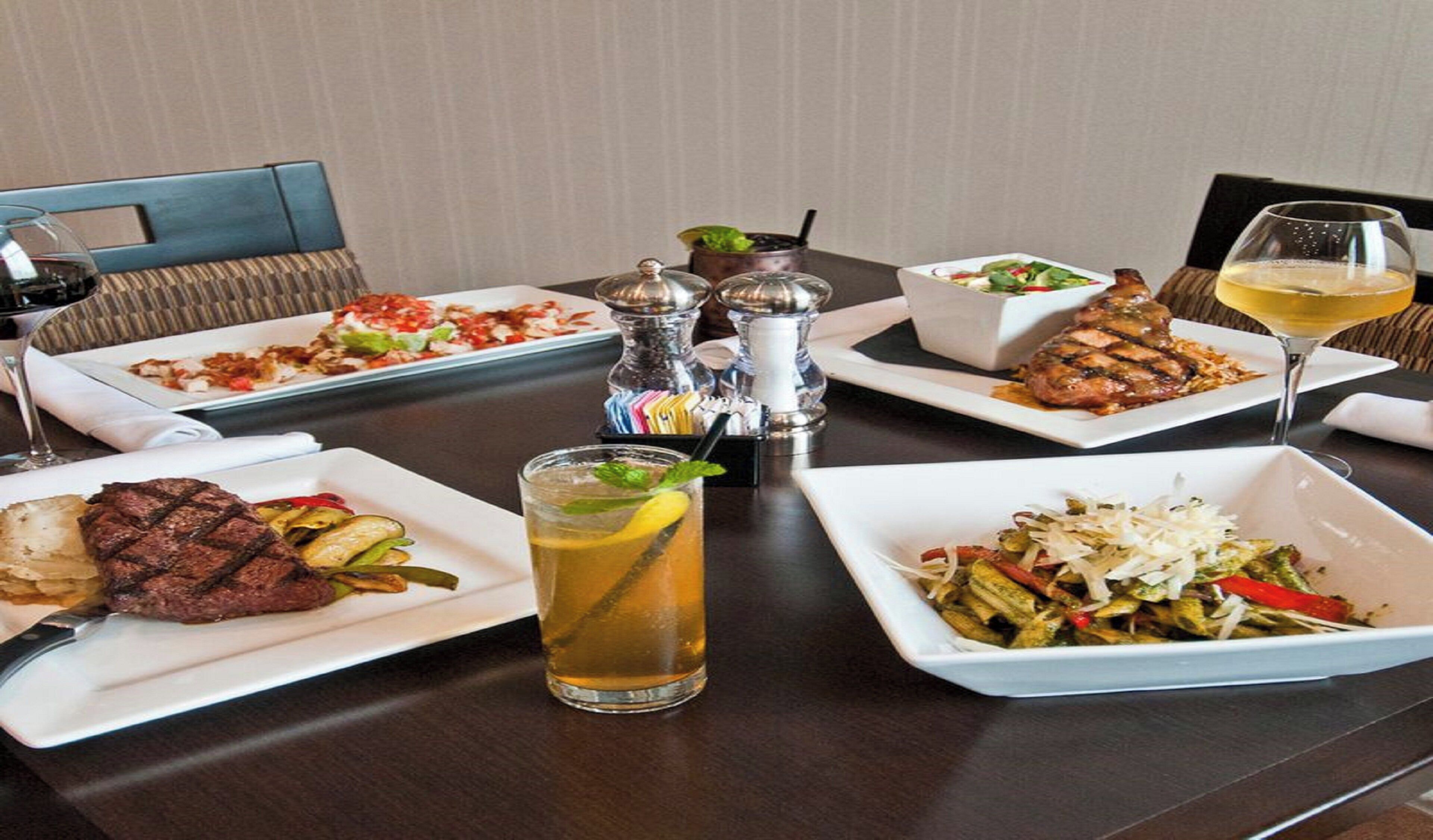 Una mesa de comedor con varios platos, una copa de vino y un cóctel.