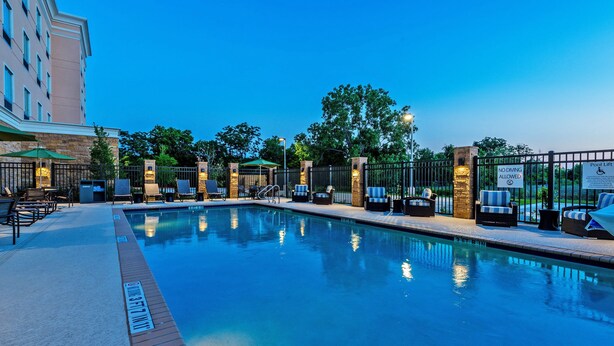 A swimming pool with lounge chairs and umbrellas, surrounded by a fence and trees. - Holiday Inn Austin Airport by IHG (Austin)
