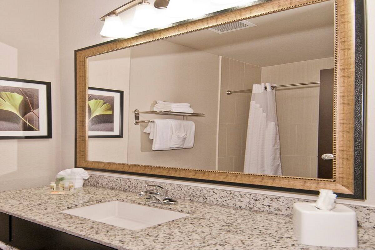 A bathroom with a large mirror, framed by a gold border, a sink with a marble countertop, and a towel rack with folded towels.