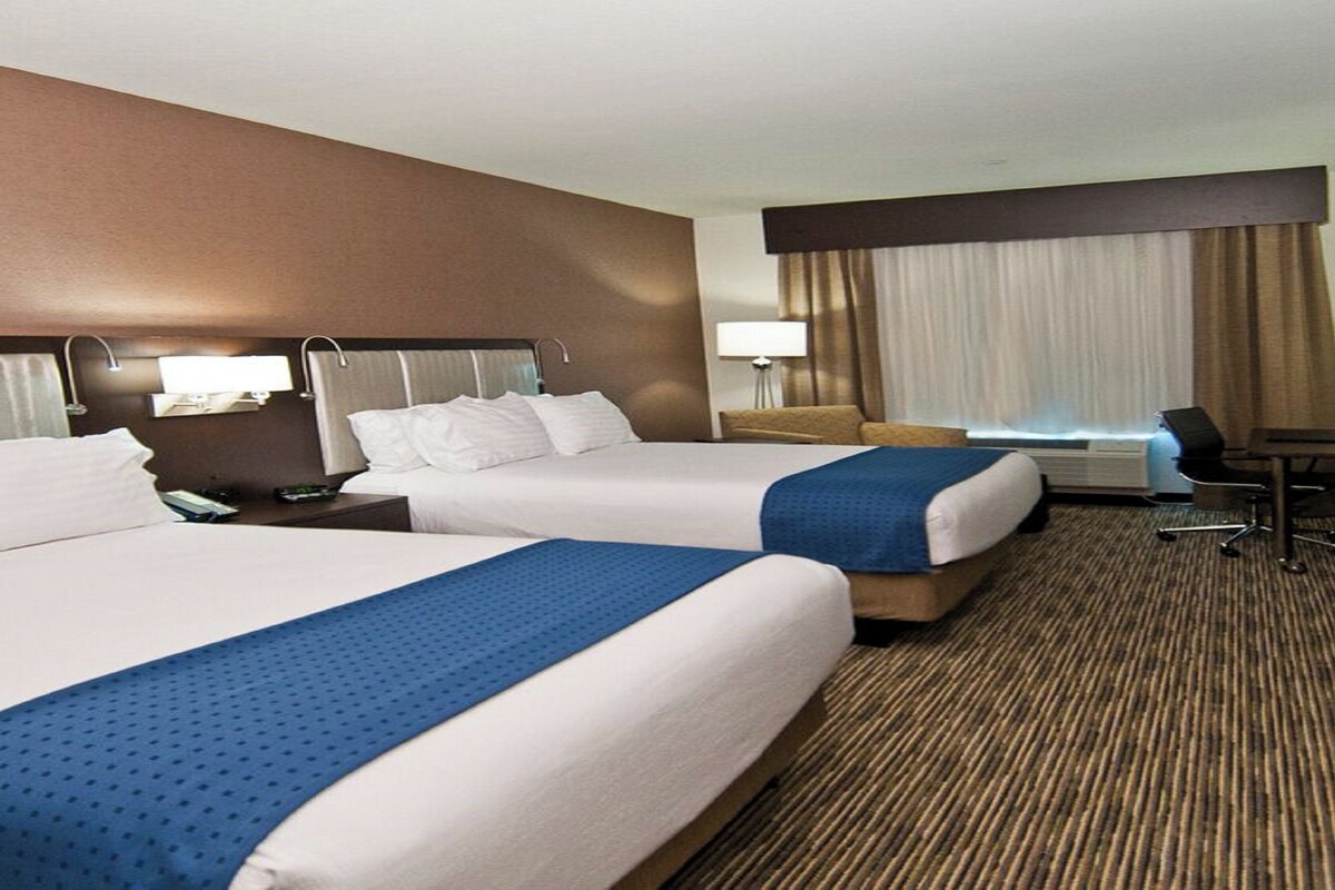 Een hotelkamer met twee bedden, een bureau, een stoel en een groot raam met gordijnen.