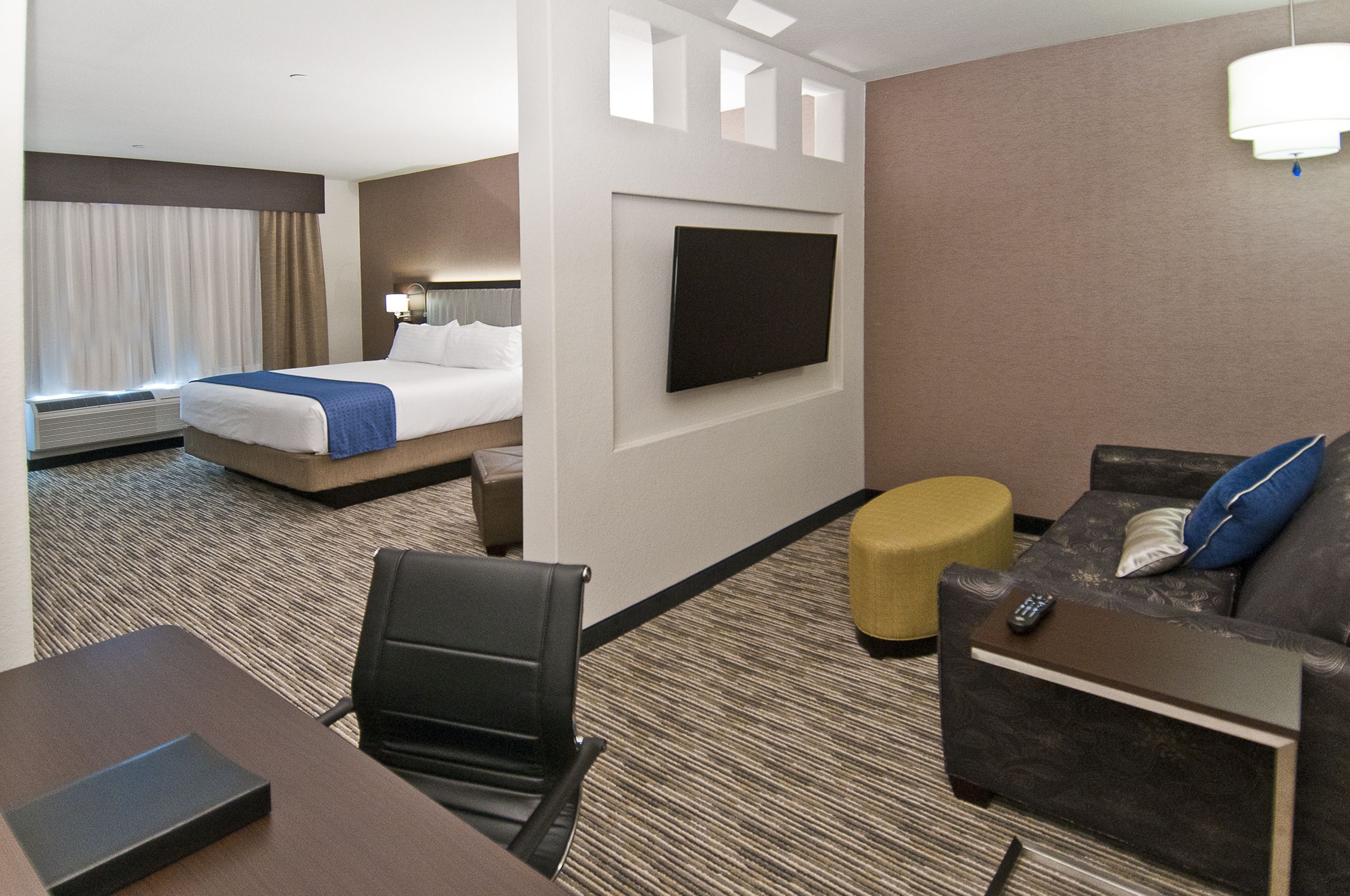 A hotel room with a bed, a TV mounted on the wall, a sofa, a small table, and a chair.