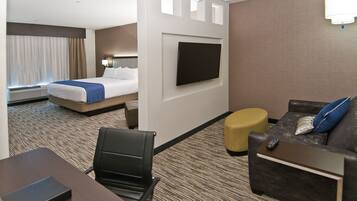 A hotel room with a bed, a TV mounted on the wall, a sofa, a small table, and a chair.