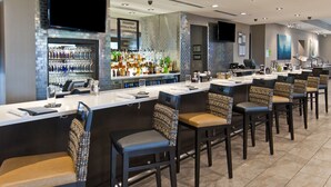 A bar area with a long counter, multiple bar stools, and a variety of bottles and glasses on shelves. - Holiday Inn Austin Airport by IHG (Austin)