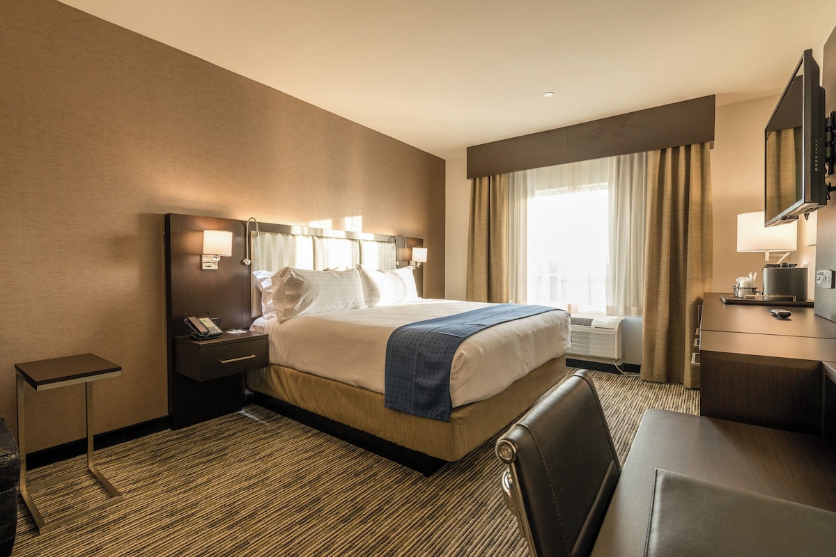A hotel room with a bed, bedside tables, a desk, a chair, a television, and a window with curtains.