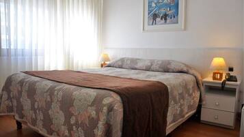 A neatly made bed with a floral bedspread, two bedside lamps, a nightstand with a telephone, and a framed picture on the wall.